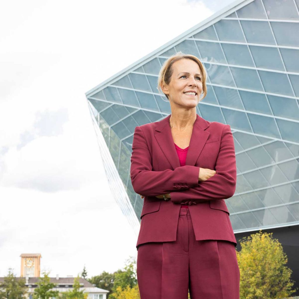 Eine Frau - Eva Döhla - in einem roten Hosenanzug vor einer modernen Halle.